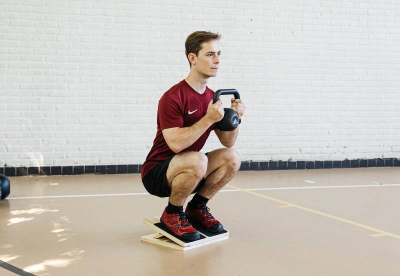 an athlete doing a slant board goblet squat for ankle stability