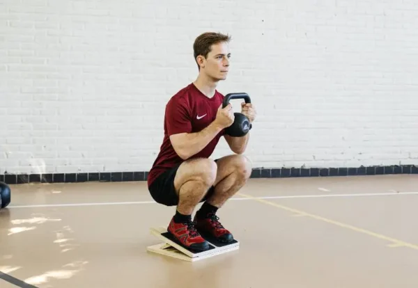 An athlete in deep squat, using a slant board for mobility